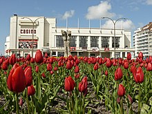 Photographie en couleur de la façade blanche du casino de Knokke-Le-Zoute ; au premier plan, un large champ de tulipes rouges.