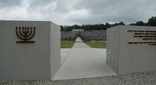 Inscriptions en hébreu, en polonais et en anglais sur un mur en pierre blanche. La base du mur présente de longues stries verticales comme s'il avait été griffé.