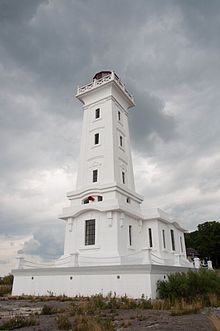 A white tower sitting on a rocky piece of land with sparse vegetation