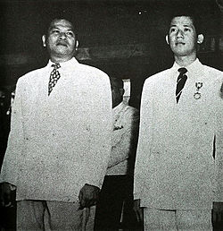 בניגנו אקינו כקצין צעיר (ימין) ושר ההגנה רמון מגסייסיי (משמאל), 1951