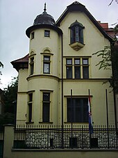 Older yellow house with low wrought-iron fence in front