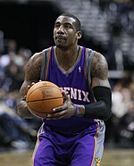 A man wearing a purple jersey with a word "PHOENIX" written in the front, is holding a basketball.