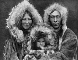 Inupiat-perheen äiti ja isä sylissään noin 6-vuotias poika. Kuvattu vuonna 1929. Perheenjäsenillä on päällään hupulliset turkikset. Vanhemmat hymyilevät, poika on vakava.