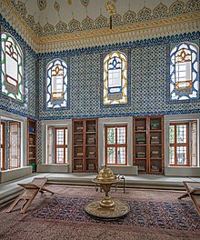 salle décorée de carrelage bleu ; trois arches ; des divans au sol