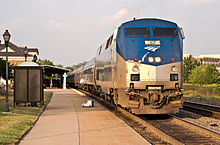 Big shiny train facing us, at station with passengers on platform