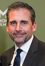 Un homme aux cheveux noirs, Steve Carell, est debout dans un smoking. Il regarde vers la caméra et sourit.