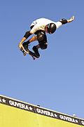 Photo de Tony Hawk durant un saut dans une rampe. Il est en l'air, regroupé sur sa planche et effectue un grab.