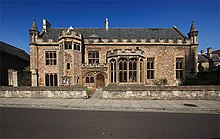 Red brick building with small tower to the left of the arched doorway and bay window to the right.