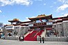 An Eastern temple with red stairway leading up to it, against a blue sky with cumulus clouds