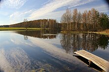 Vue depuis la rive d'un étang avec une petite jetée en bois. Des arbres qui ont perdu leurs feuilles entourent l'étang.