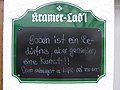 Cedule obchodu v Rottach-Egern v Bavorsku. Zvrchu je německy napsáno: Essen ist ein Bedürfnis, aber genießen eine Kunst!! (česky: Jídlo je nutnost, ale pochutnat si na něm je umění!!). Pod tím je bavorsky napsáno: Drum schaugst a bißl rei zu uns! (Proto se k nám přijď podívat!).