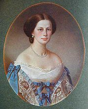 A colorful portrait of an adult woman, finely dressed and wearing jewelry, with brown hair, looking directly at the artist