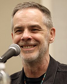 A blue duotone headshot photo of a white man with a short haircut in T-shirt.