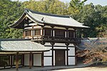 Two-storied wooden building with white walls and an attached open veranda with handrail on the upper floor.