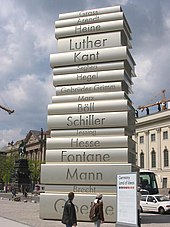 ein Stapel von übergroßen Büchern aus Metall; der Turm ist über 10 Meter hoch und etwa 4 Meter breit; die Titel großer Autoren sind auf den Buchrücken sichtbar