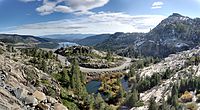 Vista of mountain pass with pine trees, curving road, and lake in background