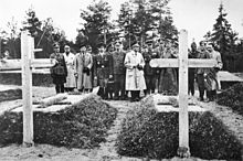 17[ölü/kırık bağlantı] men, most in military uniform, stand in a cemetery, inspecting two graves.