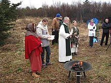 Eight people, all white, stand on heathland. Some of them are dressed in historical clothing akin to that worn in the medieval period.