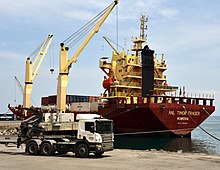 Red and yellow cargo ship being unloaded by cranes