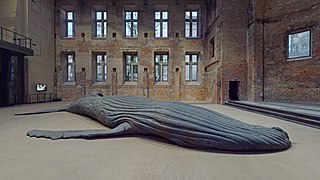 Socha mrtvého keporkaka ze zřetelně sploštělým tělem na zemi v budově připomínající továrnu