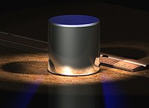 Компьютерное изображение международного прототипа килограмма, рядом изображена дюймовая линейка. По размерам он сопоставим с мячом для гольфа, края имеют фаски для минимизации износа материала