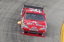 A red race car turning left and spouting out a flame from its right-hand exhaust pipe