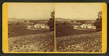 Two nearly identical images side by side in stereograph format of a small 19th century college campus. In the foreground are neatly planted rows of crops. The nearest building is an ornate 19th century conservatory or greenhouse. In the distance, on a ridge, are three brick academic buildings.