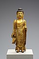 Statuette dorée représentant un bouddha debout, les yeux fermés, une main le long du corps et l'autre tenant un bol.