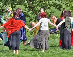 Eine Gruppe Wiccas bei einem Ritual. Sie halten sich an ihren Händen und bilden einen Kreis.