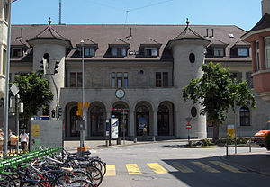 Three-story building with gabled roof and turrets flanking the entrance