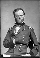 Black and white photo of a frowning bearded man with his right hand tucked into his coat. He wears a dark military uniform.