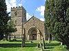 A church between trees with its tower on the left and a Norman doorway to the right