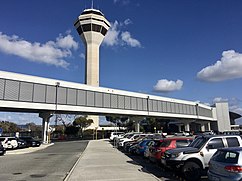 Enclosed footbridge passing over carpark with airport control tower in the background