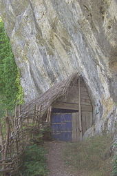 Photo montrant une hutte située contre la falaise et couverte de branchages.
