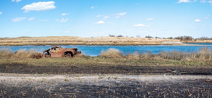 Au bord d'un chemin perdu, une avancée d'eau vide, dans un paysage sans aucun immeuble, une carcasse de voiture abandonnée.