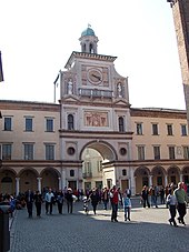 A large, three-story, beige-and-white building that has a central domed clock tower with an arch beneath.