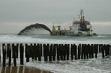 photo depuis une plage, un navire passe près de la plage en projetant du sable.