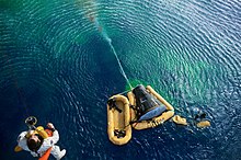 Photograph of the Gemini 10 spacecraft in the ocean and Young being hoisted from it