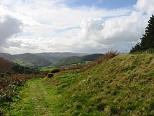 Photo d'un paysage rural herbeux. Le terrain s'élève sur la droite.