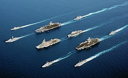 La photographie montre le Stennis dans la mer d'Oman, entouré d'un cortège de porte-avions, de croiseurs et de frégates.