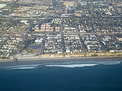 Aerial view of part of old town Encinitas showing Moonlight Beach on the left. Parallel with the shore is Historic Coast Highway 101, also parallel and further inland is Interstate 5 in California
