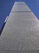 Aerial view of two 110-story twin towers; the building have gray, steel exteriors, and the structure on the left is topped by a large antenna. Several skyscrapers are visible surrounding the two towers.