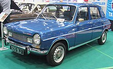 Une Simca 1204 bleue vue de trois quart avant, présentée sur une estrade basse dans un salon automobile.