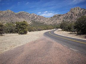 State Highway 166 winds toward Sawtooth Mountain in the distance. Thick growths of shrubs and small trees are along both sides of the road. Sawtooth Mountain has rugged outcrops of rock at its summit giving the mountain its name. Shrubs partially cover the mountains flanks.