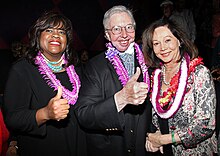 Three people are smiling with Hawaiian leis around their necks.