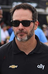 A man in his early forties wearing black sunglasses and sporting a graying beard.