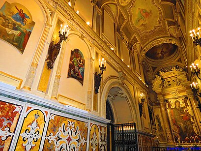 A picture of the basilica inside the Abbey of Montevergine. It is a long hallway bathed in warm candlelight, and Renaissance-era depictions of Mother Mary's life.