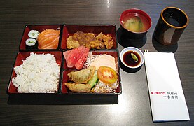 Bento sing kalebu salmon sashimi, teriyaki pitik lan gyoza, disajikake ing restoran Jepang ing Jakarta .