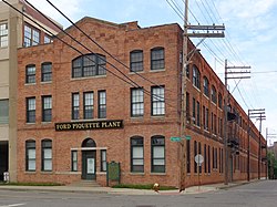 A three-story brick building with late Victorian-style architecture. A row of telephone poles are on the right and a historical marker is next to the front door.