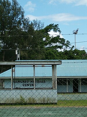 An empty netball court in front of a building with a corrugated iron roof.